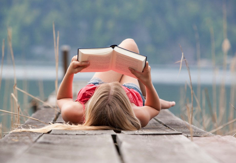 Austria, Teenage girl lying and reading book on jetty